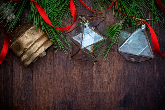 Delicate glass Christmas decorations, red ribbon and natural branches of pine (spruce) on wooden background.