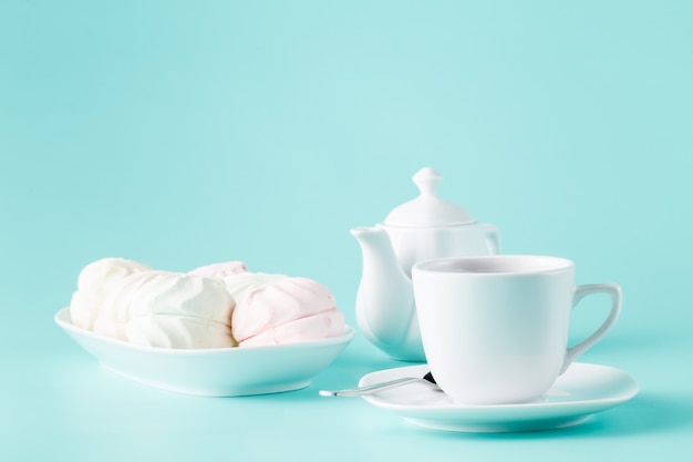 Delicate meringues, marshmallows and cup of english tea on white table