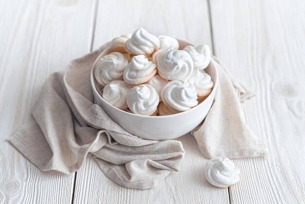 Photo delicate meringues on a white background with a cup of tea. side view.airy meringue on a light background with a napkin.