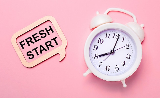 On a delicate pink background a white alarm clock and a wooden frame with the text FRESH START