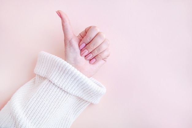 Delicate pink manicure A woman's hand in a white sweater on a pink background Nude shade of gel polish top view copy space Elegant design