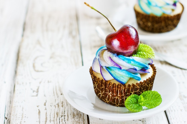 Delicate vanilla cupcakes with cream and berries on white wood