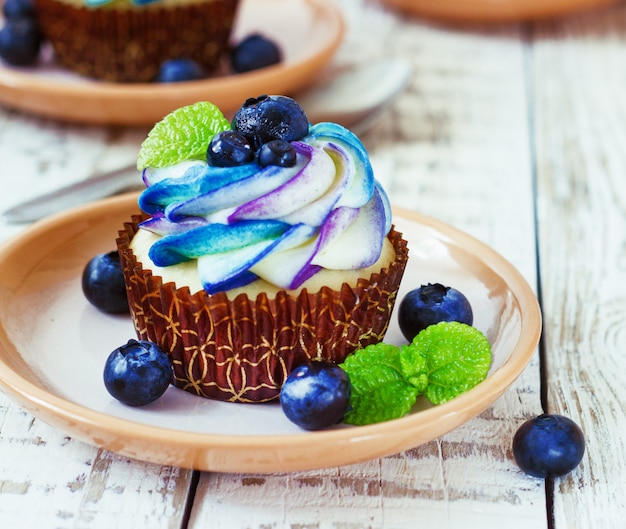 Delicate vanilla cupcakes with cream and berries on a white wooden