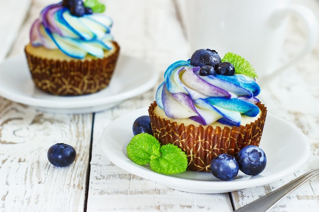 Delicate vanilla cupcakes with cream and berries on a white wooden