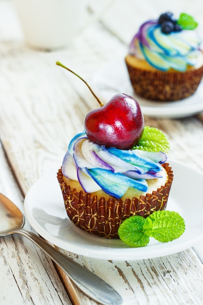 Delicate vanilla cupcakes with cream and berries on a white wooden