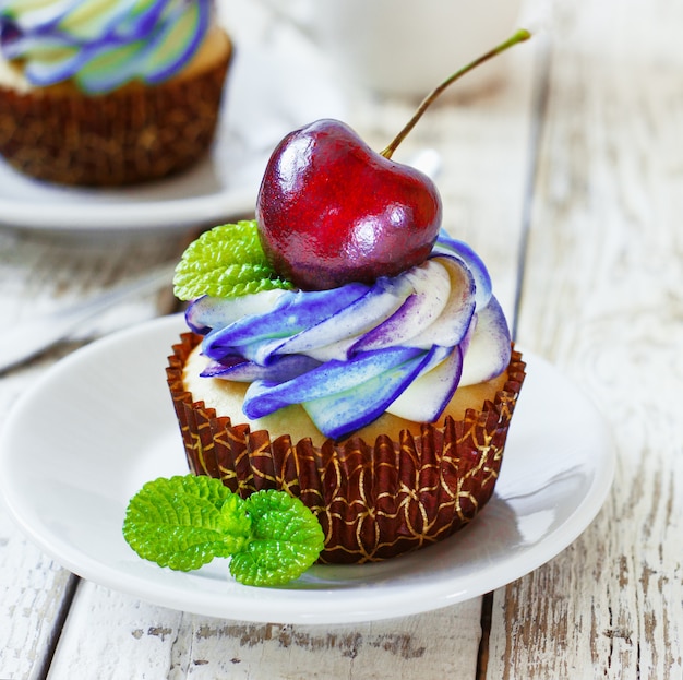 Delicate vanilla cupcakes with cream and berries on a white wooden