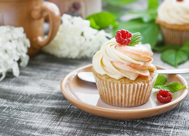 Delicate vanilla cupcakes with cream and raspberries on a dark wooden surface