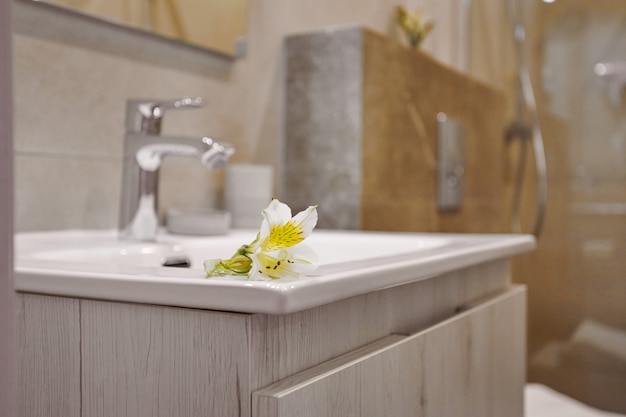 A delicate white flower lies on the edge of the sink with a shiny tap