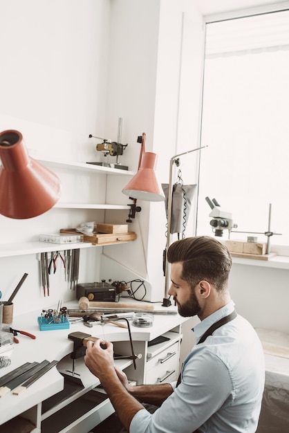 Delicate work side view of male jeweler making a silver ring with professional adjustable jewelers