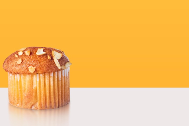 Photo delicious almond topped cupcake muffin with reflection on white table with yellow background