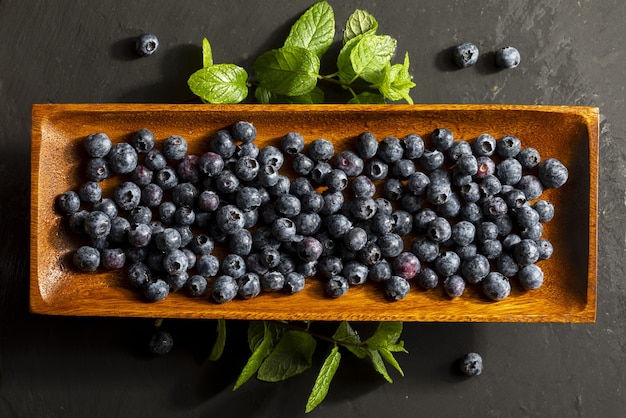 Delicious and appetizing blueberry berries on an ebony wood tray and mint leaves (peppermint, mint)