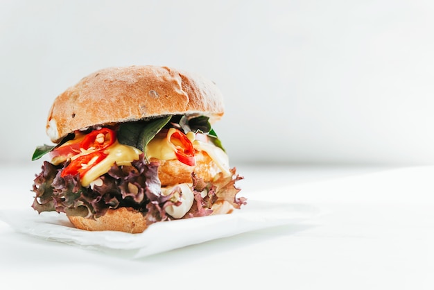 Delicious and appetizing burger with chicken cutlet, basil and chili pepper on a white wooden background