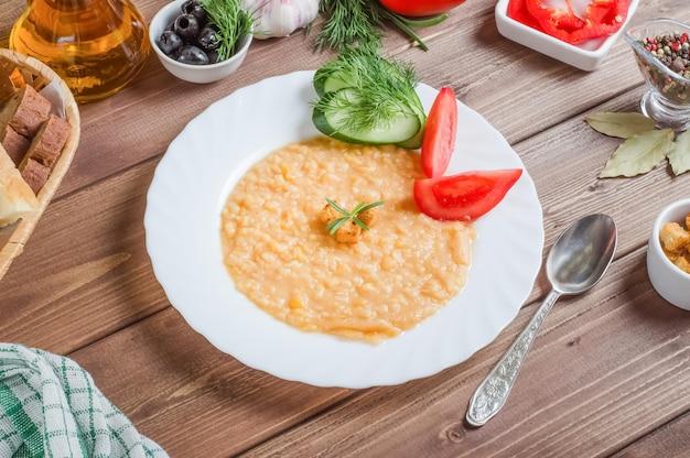 Delicious appetizing pea porridge garnish with fresh vegetables on a white plate on a wooden background