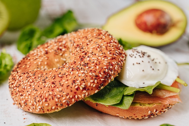 Delicious bagel with sesame and chia bread, inside it contains salmon, fried egg and basil.