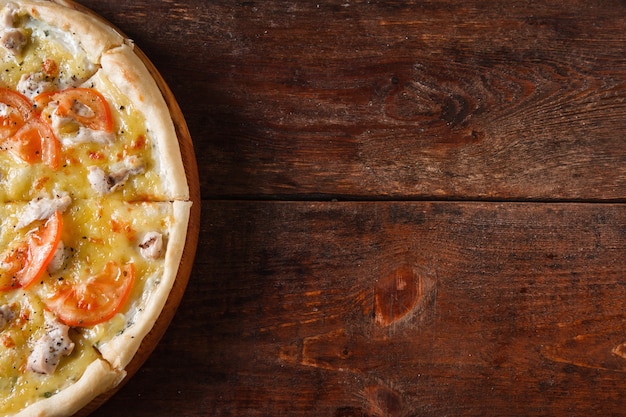 Delicious baked pizza with chicken, tomatoes and cheese served on wooden table, flat lay. Dark background with copy space.