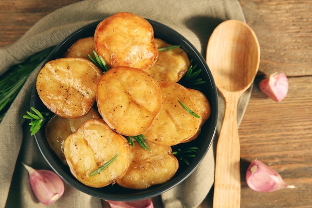 Delicious baked potato with rosemary in bowl on table close up