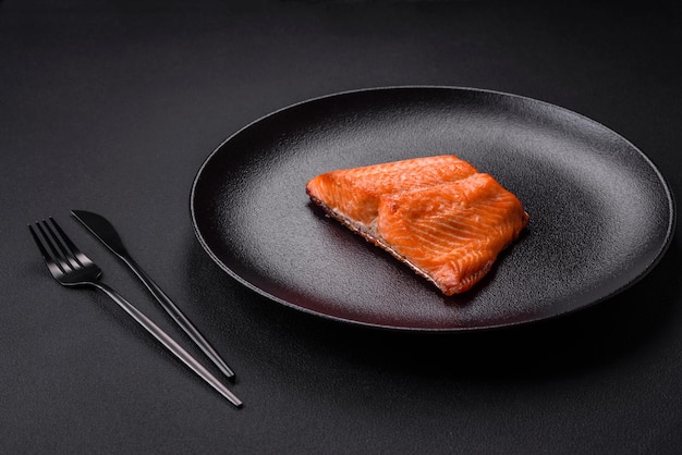 Delicious baked salmon red fish steak with spices and herbs on a dark concrete background