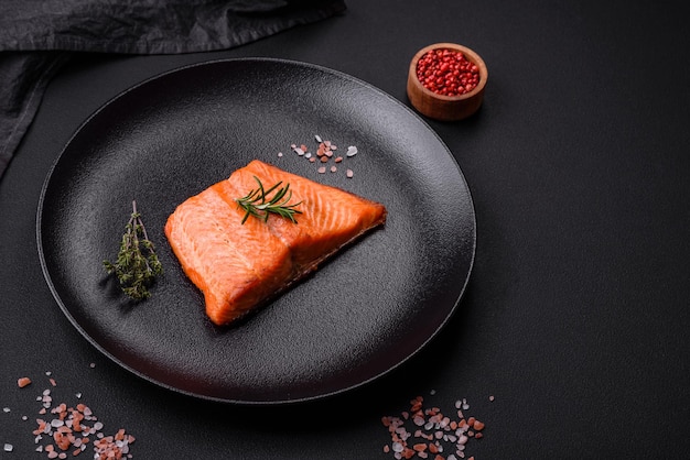 Delicious baked salmon red fish steak with spices and herbs on a dark concrete background