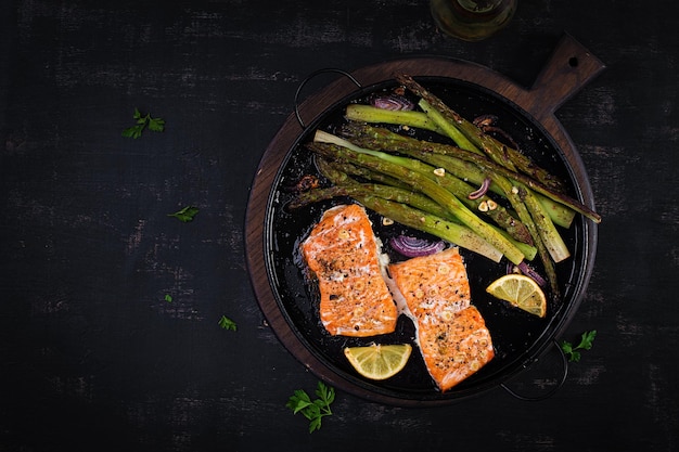 Delicious baked salmon with asparagus lemon slices and spices on dark table Top view flat lay