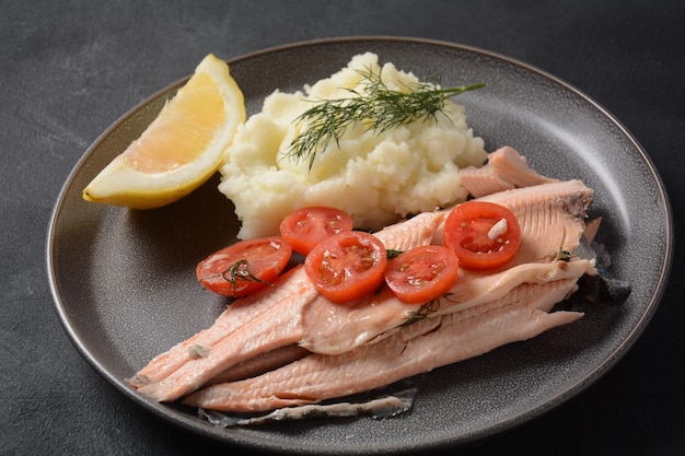 Delicious baked trout with cherry tomatoes olive oil lemon juice and fresh dill on white plate with lemon slices