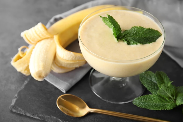 Delicious banana homemade smoothie in dessert bowl on grey background