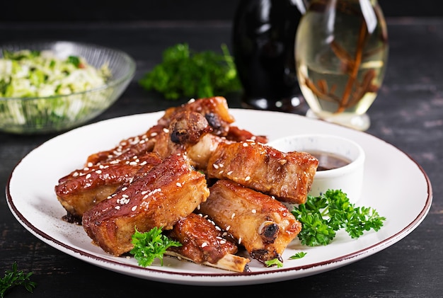 Delicious barbecued spare ribs on plate on dark background Tasty bbq meat