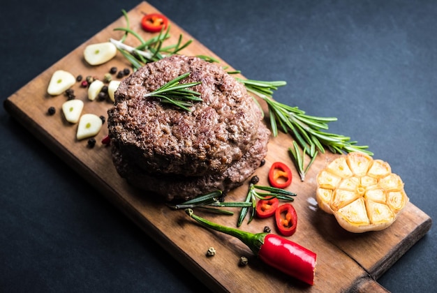 Delicious beef burger steak with spices and herbs on cutting board and slate background top view