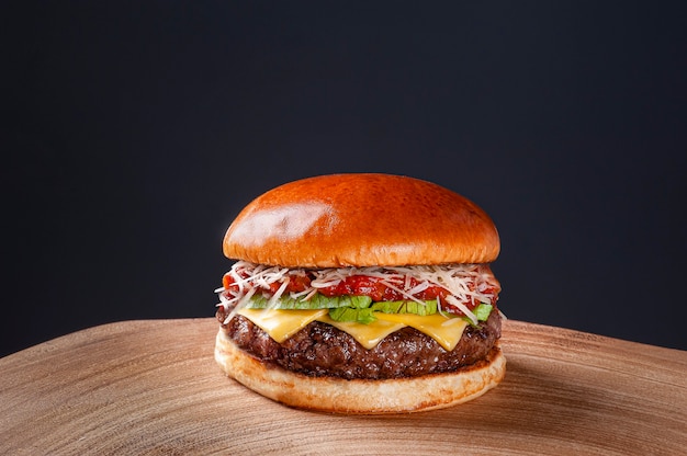 Delicious beef burger with tomato sauce, parmesan cheese and lettuce on wooden table on dark background. Copy space