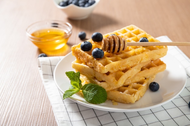 Delicious Belgian waffles on a plate with honey and fresh blueberries