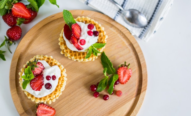 Delicious belgian waffles with wipped cream and strawberries on round wooden plate overhead flat lay