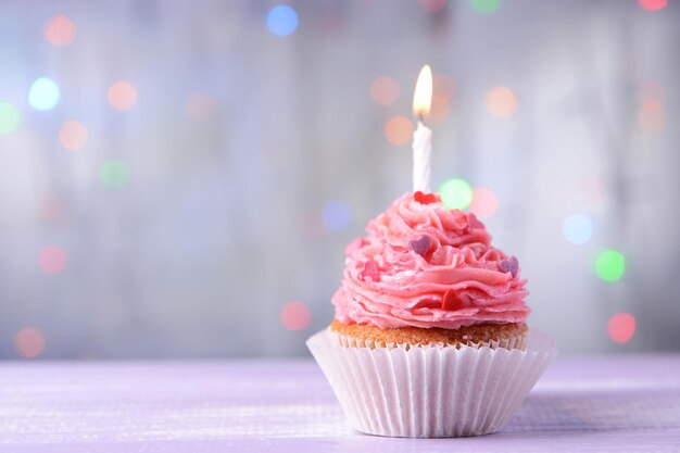 Delicious birthday cupcake on table on light background