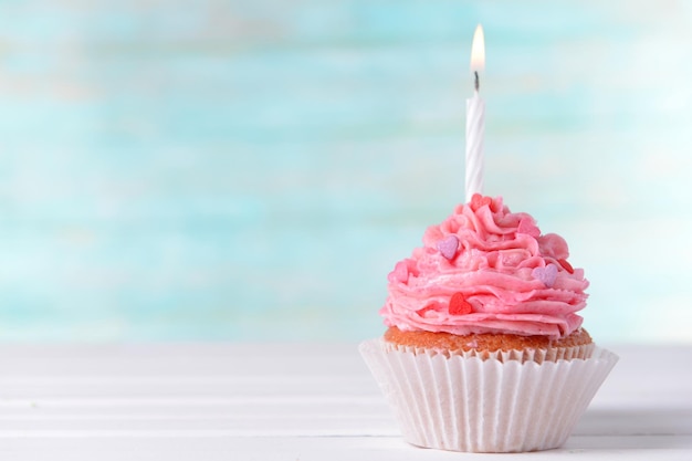 Delicious birthday cupcake on table on light blue background