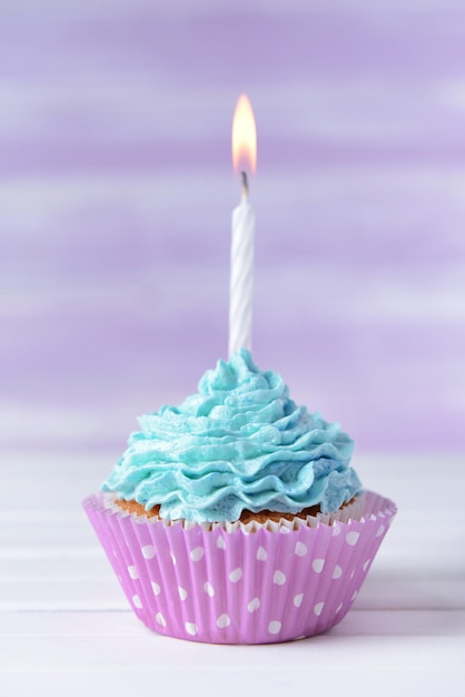 Delicious birthday cupcake on table on light purple background