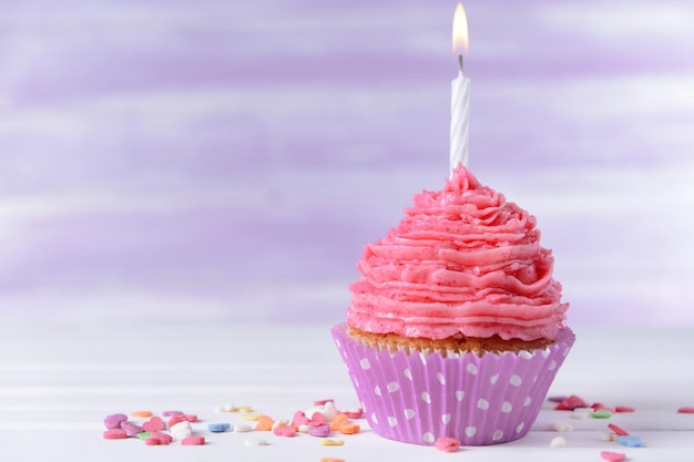 Delicious birthday cupcake on table on light purple background