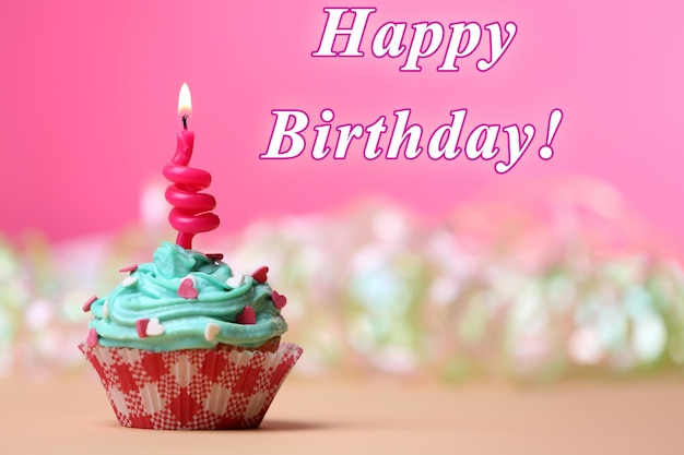 Delicious birthday cupcake on table on pink background