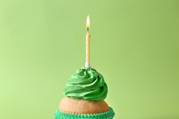 Delicious birthday cupcake with burning candle on color background