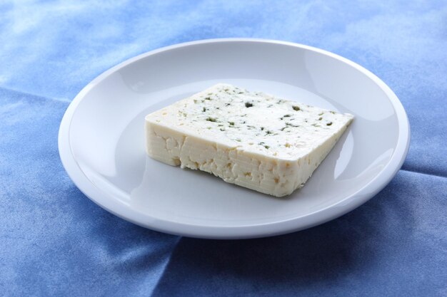 Delicious blue cheese on a white plate and blue background Closeup of a slice of dorblu cheese Blue cheese under spotlight