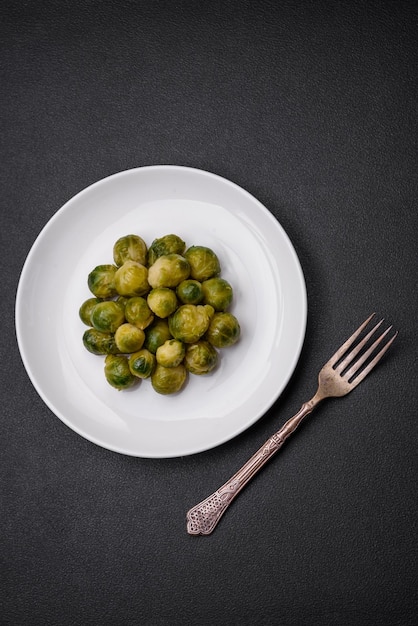 Delicious boiled Brussels sprouts on a ceramic plate on a dark concrete background