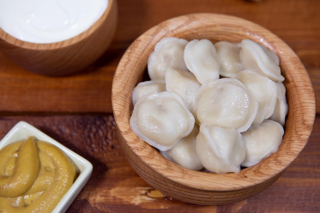 Delicious boiled dumplings on a wooden background with mustard sauce sour cream and bread