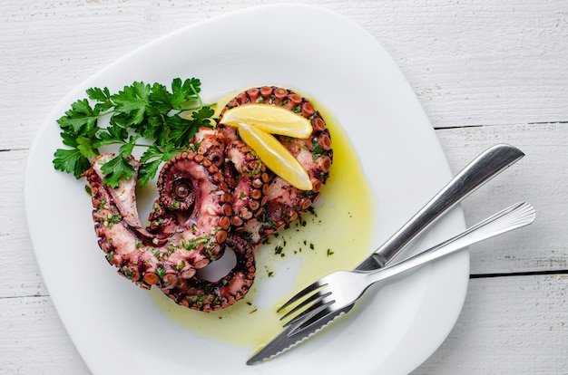 Delicious boiled octopus with lemon ,parsley and salad dressing on white plate.