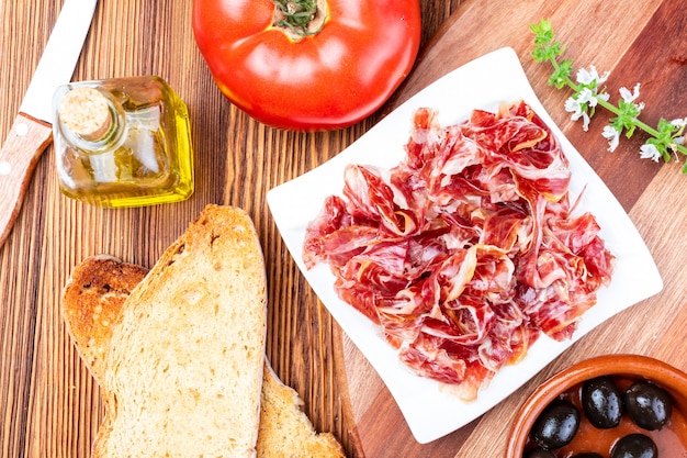 Delicious bread toast with natural tomato, extra virgin olive oil, Iberian ham, black olives and basil leaves.