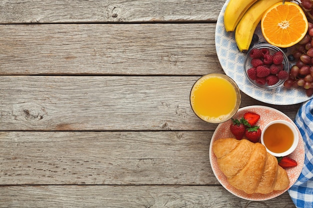 Delicious breakfast background. Tasty croissants, muesli and fresh sweet organic berries for morning meals on rustic wooden table with copy space. Top view on rich everyday nutrition