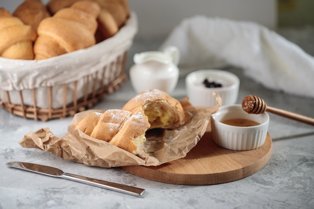 Delicious breakfast, close-up. A broken croissant with cream lies on a wooden board, with a honey bowl and a jug of cream.