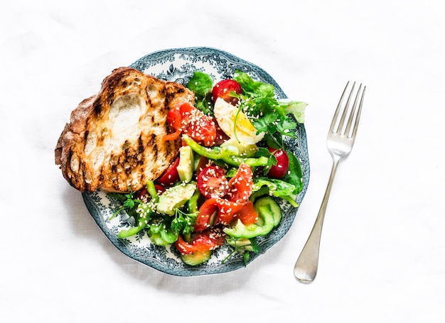 Delicious breakfast snack salad with salmon egg vegetables lettuce and grilled bread on a light background top view