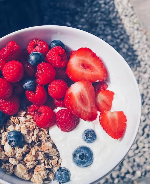 Delicious breakfast with cereal yogurt strawberries raspberries and bluberries in the garden outdoors healthy food and diet