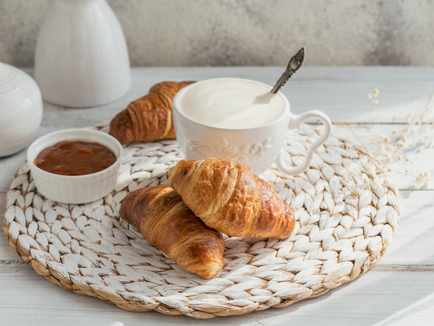 Delicious breakfast with fresh croissants and cup of coffee served with jam on a white wooden. Delicious Baking