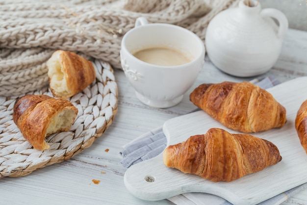 Delicious breakfast with fresh croissants and cup of coffee on a white wooden