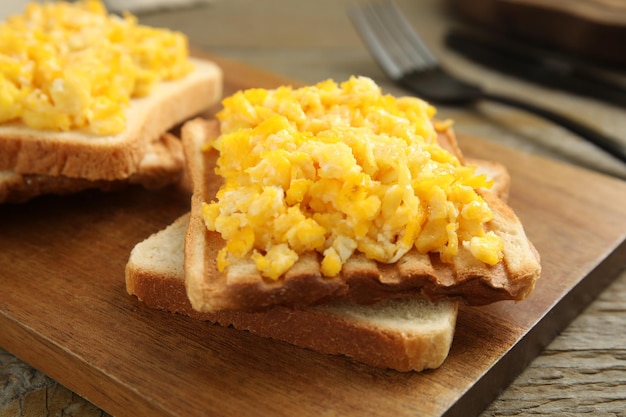 Delicious breakfast with scrambled eggs and toasted bread served on wooden board closeup