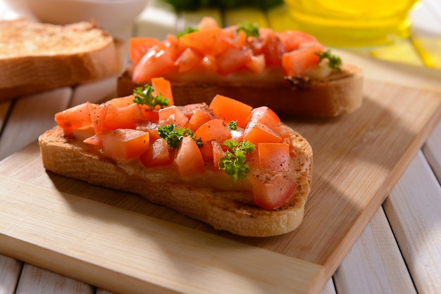 Delicious bruschetta with tomatoes on cutting board closeup