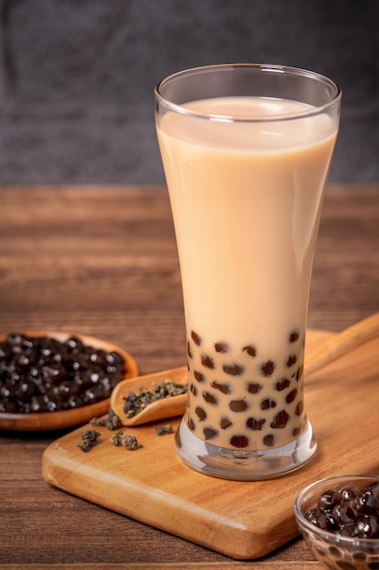 Delicious bubble milk tea with tapioca pearl ball in glass on wooden table and dark gray brick background popular food and drink in Taiwan close up